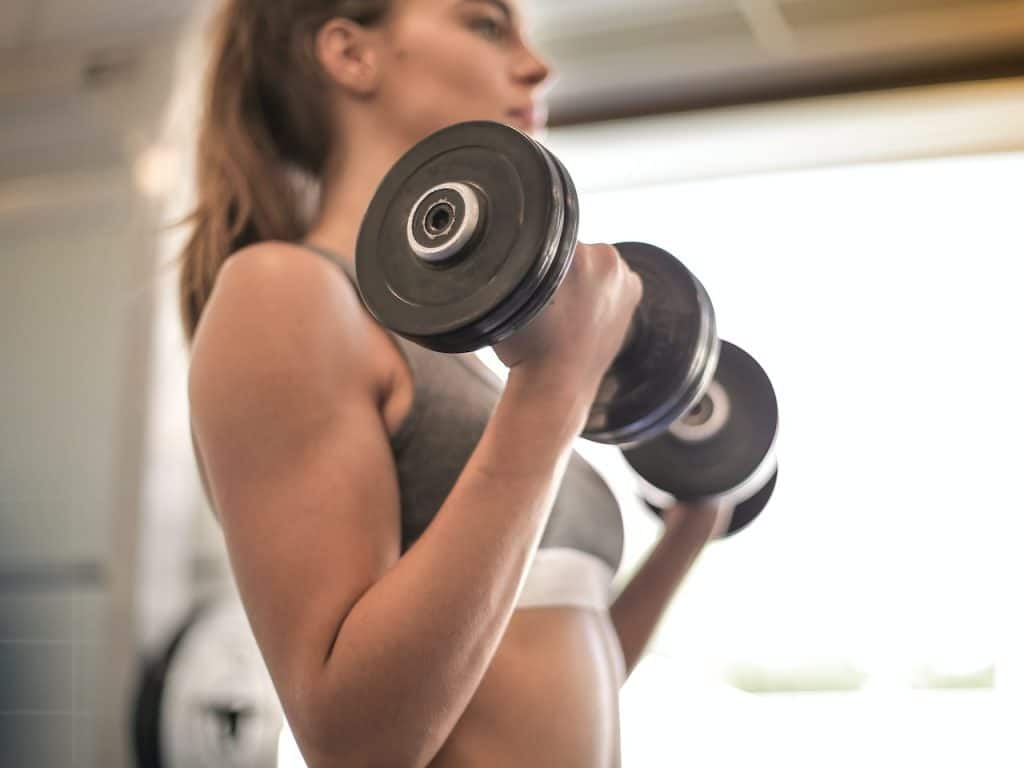 Mujer que toma caseína para mejorar su músculo, entrenando con mancuernas.