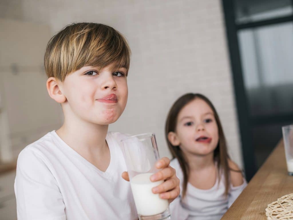Niños beben leche que es un alimento con calcio.