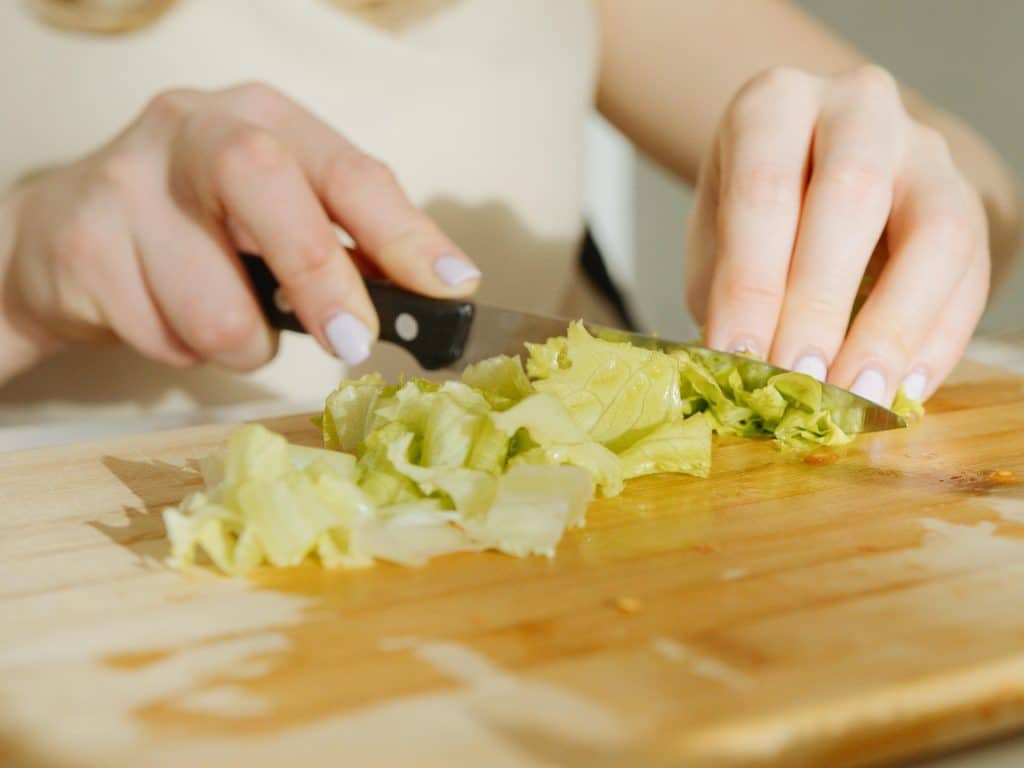 Mujer corta una lechuga sobre una tabla de madera