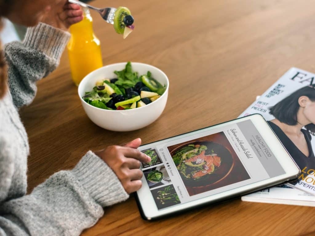 Mujer come ensalada y mira una tablet