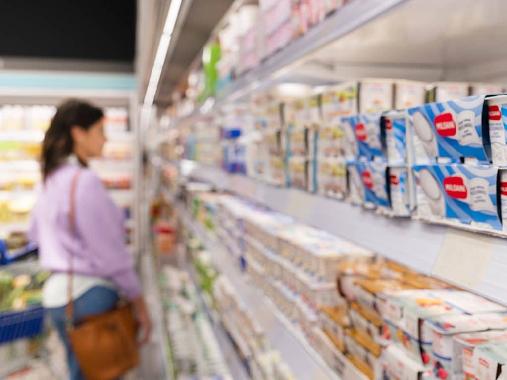 Mujer comprando en lineal de un supermercado y mirando etiquetas de información nutricional